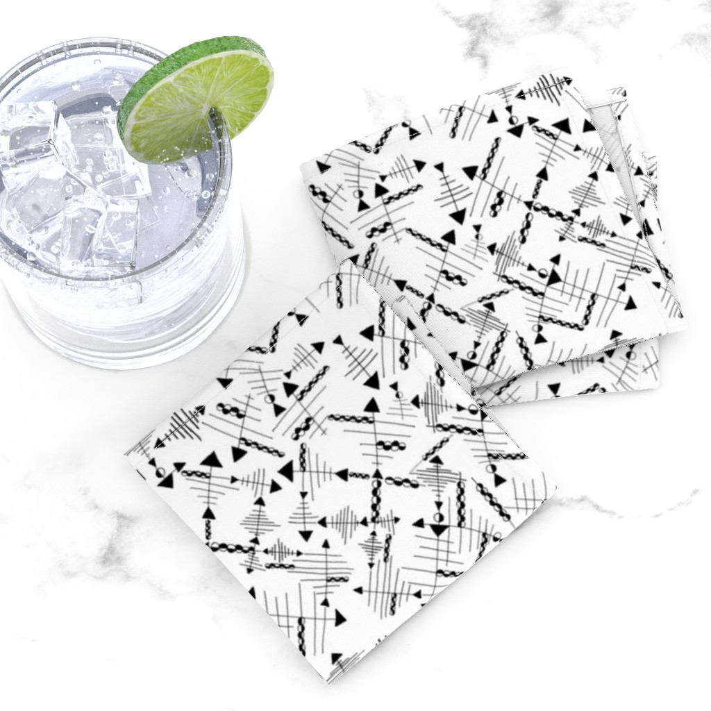 Top down of two folded Cocktail Napkins overlapping next to a glass tumbler full of ice and liquid with a lime wedge on a white marble tabletop
