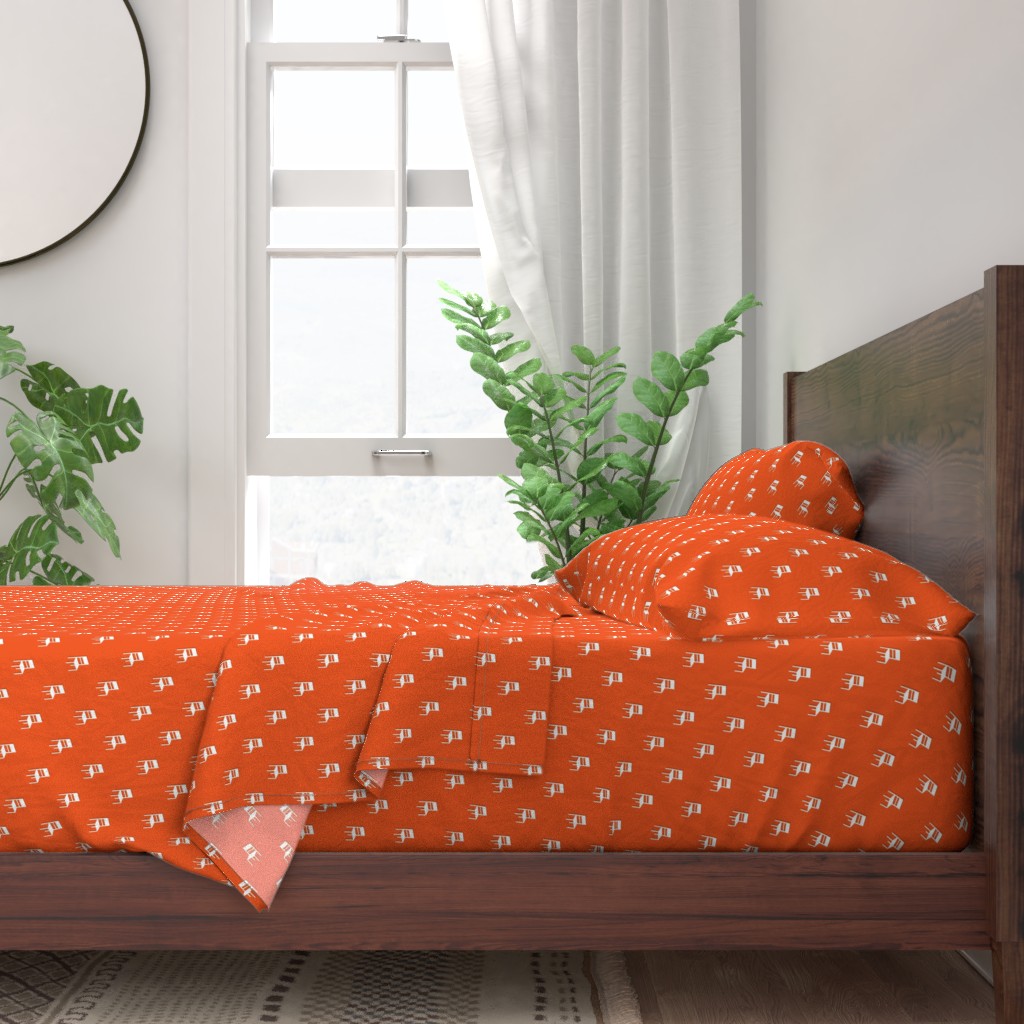 A neatly made bed with sheets and pillows with a wooden bedframe. The bed is next to a window with plants on either side and a round mirror hangs on the wall to the left of the window.