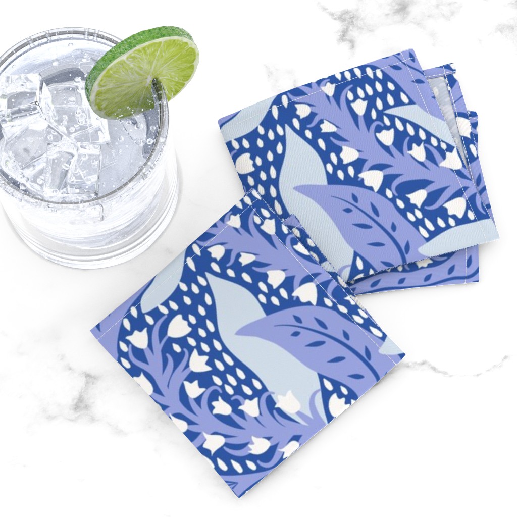 Top down of two folded Cocktail Napkins overlapping next to a glass tumbler full of ice and liquid with a lime wedge on a white marble tabletop
