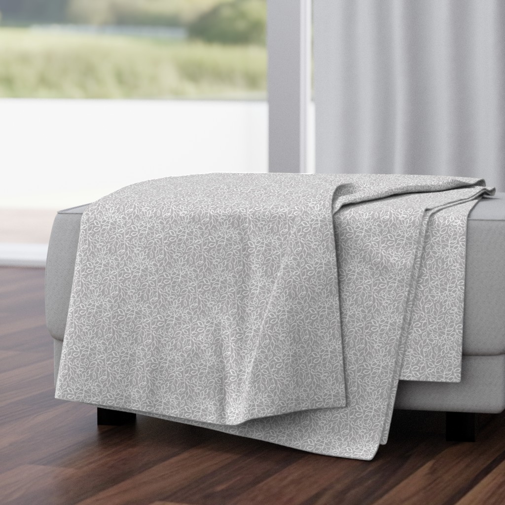 Folded Throw Blanket draped over a plush fabric ottoman in a living room in front of an open window with dark wood floors.