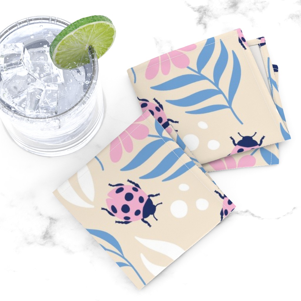 Top down of two folded Cocktail Napkins overlapping next to a glass tumbler full of ice and liquid with a lime wedge on a white marble tabletop